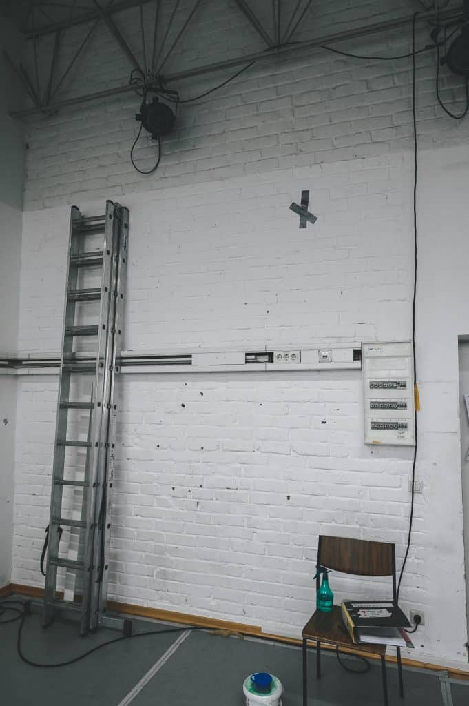 DE: Bühnchen. weiße Wände und Leiter. Stuhl neben der Leiter, kabel hangen von Lichtquellen oben nach unten// EN: studio. white wall and ladder. chair next to the ladder. and a cable coming from the light above.